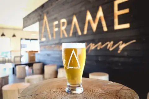 A glass of A-FRAME beer in front of the brewery's sign