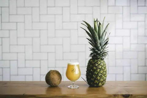 A glass of Bannerman IPA beside a pineapple and coconut