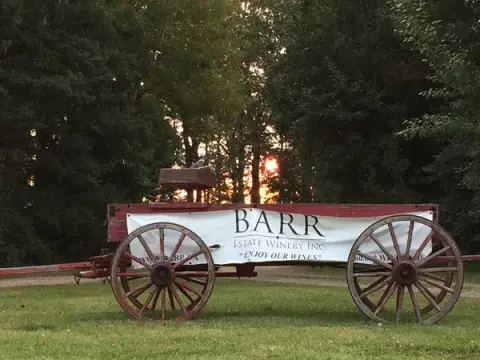 An old red wooden wagon with a Barr Estate Winery sign on the farm lawn at sunset