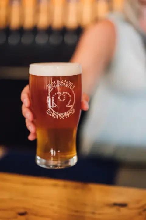 A pint of amber beer in a Beacon Brewing glass at the bar
