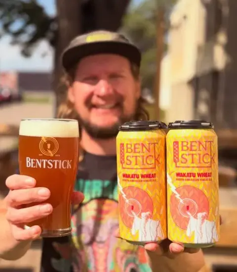 Cans of Bent Stick Wakatu Wheat beside a poured glass