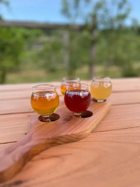A tasting flight of four ciders on a wooden paddle at the orchard