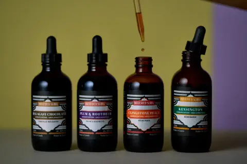4 bottles of bitters, one with the dropper open, one with the dropper out and a drop of bitters falling back into the bottle.