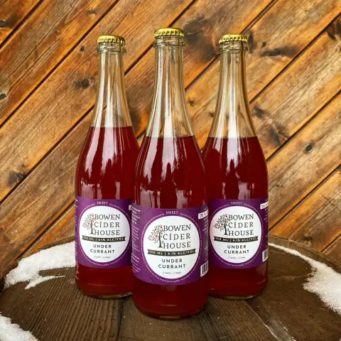 Three bottles of Bowen Cider House Undercurrant cider on a wooden table