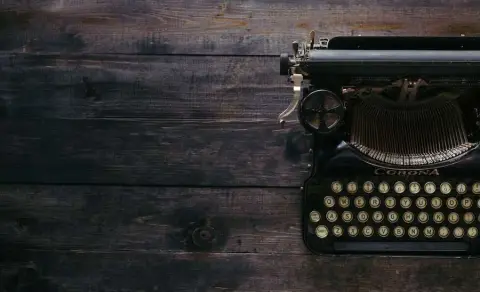 old black corona typewriter sitting on a dark wooden table top