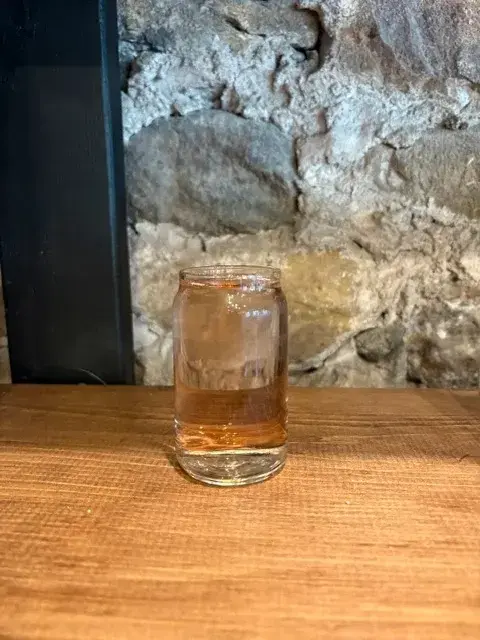 A glass of Crimson cider on a wooden table against the stone wall of the tasting room