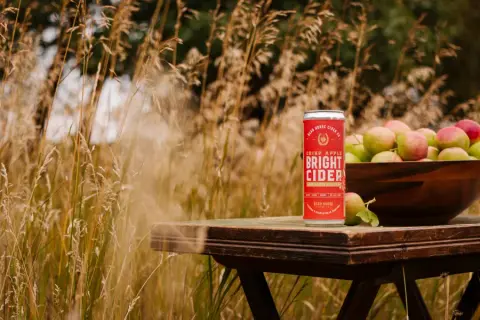 A can of Bright Cider beside a bowl of apples