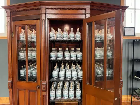Une armoire en bois avec des portes vitrées, contenant plusieurs bouteilles de spiritueux alignées sur des étagères.
