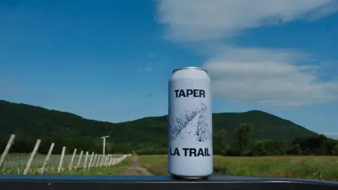 A can of Taper la trail cider in front of the vineyard and Mont Yamaska