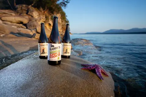 Three bottles of Gabbie's cider on a shoreline rock on Gabriola Island