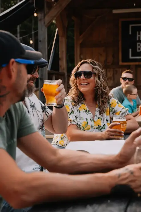 People enjoying drinks and socializing at an outdoor bar or patio area with wooden structures and string lights.