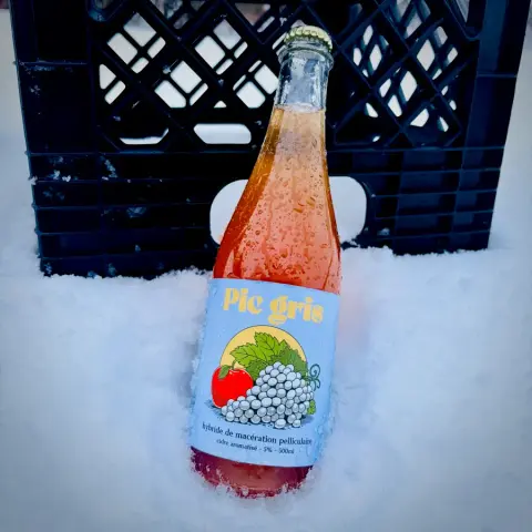 A bottle of Ibride Pic Gris cider standing in snow in front of a crate