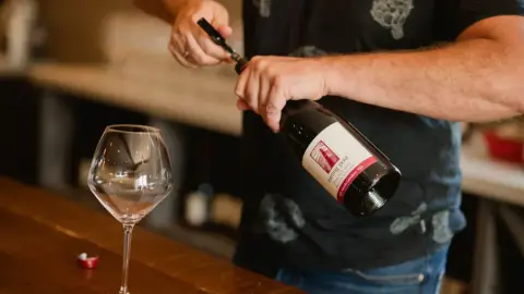 A bottle of Leaning Post wine being opened beside a glass on the tasting bar
