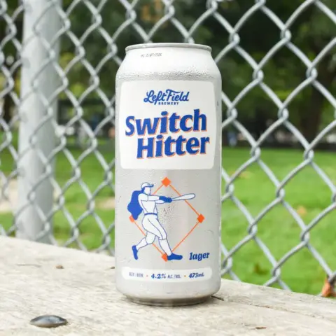 Can of Left Field Switch Hitter by a ballpark fence