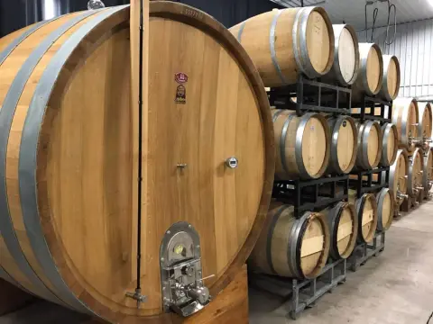Large oak wine cask and rows of stacked barrels in the cellar at Legends Estates Winery