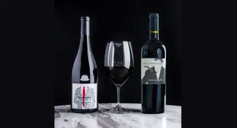 Bottles of Megalomaniac Pinot Noir and Unconventional Cabernet Merlot beside a glass of red wine