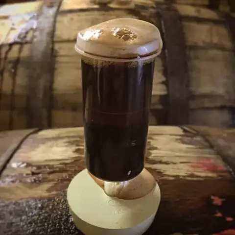 A glass of dark beer resting on an oak barrel