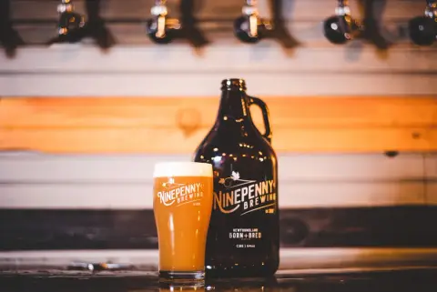 Ninepenny Brewing growler and pint glass in front of the taps