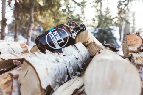 An NWT Brewing growler resting on birch logs