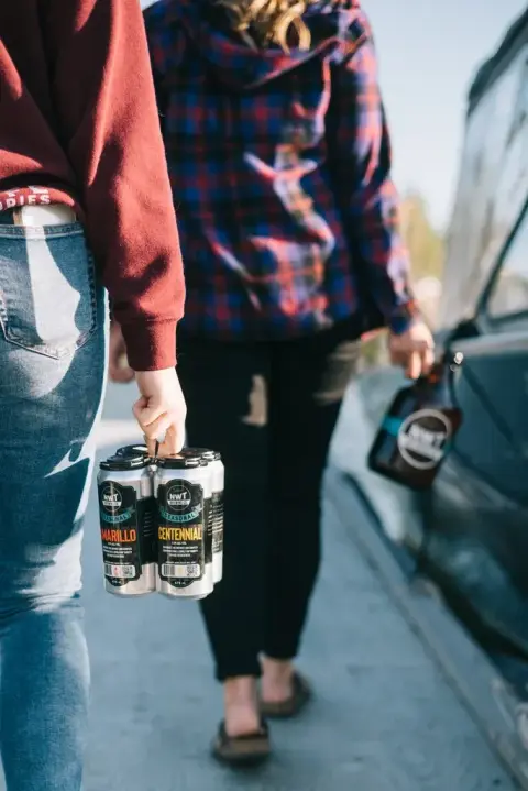 Carrying a four-pack of NWT Brewing cans and a growler