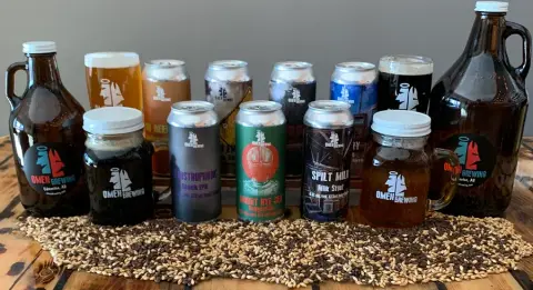 Omen Brewing cans, growlers and howlers lined up on a bed of malt