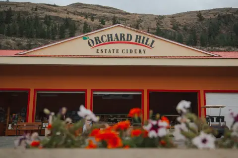Orchard Hill Estate Cidery's red-roofed farm building below the Okanagan hills