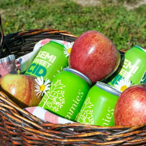 Cans of Pommies Original cider in a picnic basket with red apples