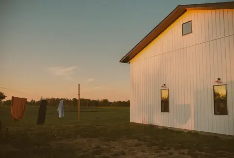 A white farm building beside open prairie field at dusk in Lac Ste. Anne County
