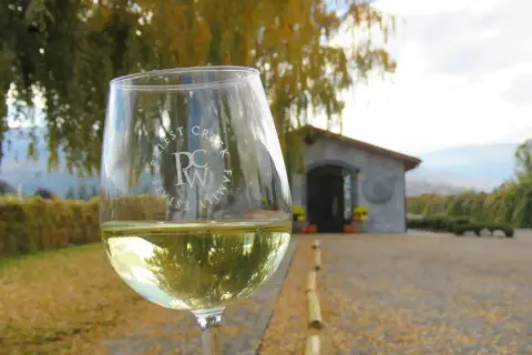 A glass of Priest Creek white in front of the stone tasting room in autumn