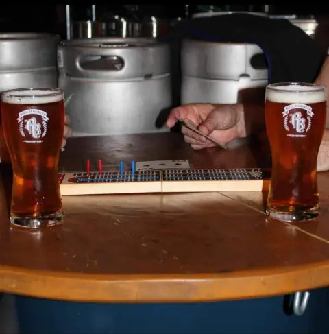 Two pints of Ridge beer on a cribbage board in front of the brewery's kegs