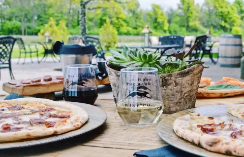 A table on the patio with wood-fired pizza and Hare glasses, vines behind