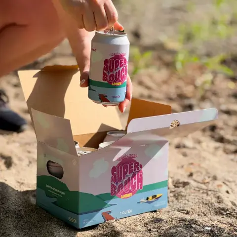 A six-pack of Super-Bouch Light cans opened on the sand